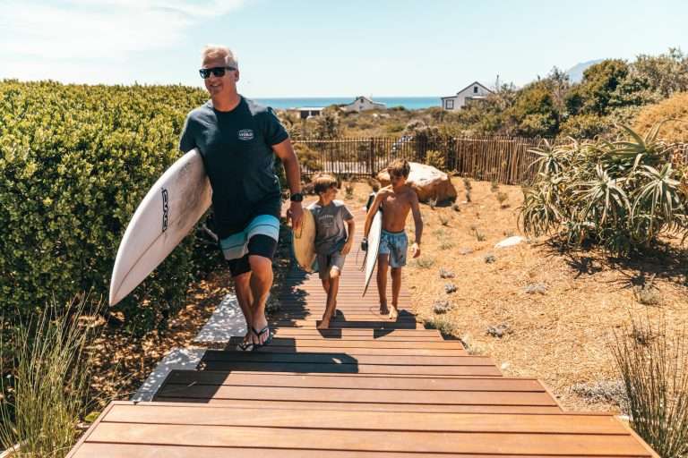 Father and sons returning from the beach with surfboards at Ballykom in Kommetjie