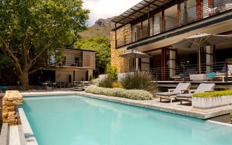 Elegant Cape Town villa with poolside loungers, garden terrace, and mountain views in the background.