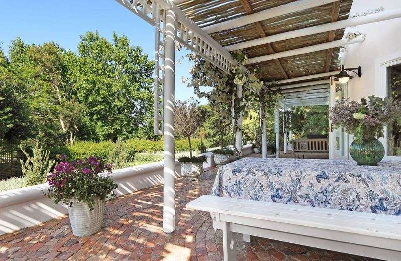 Shaded garden verandah at French Country Silo Villa with white trelliswork, potted flowers, and scenic forest surroundings.