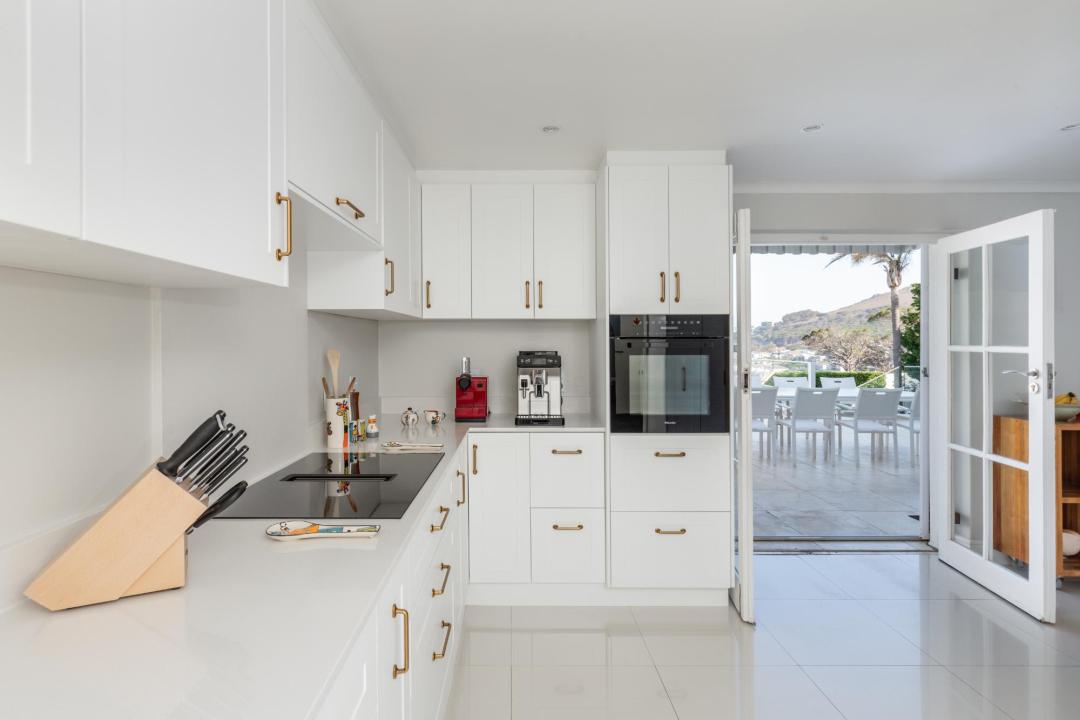 Bright modern kitchen with white cabinetry gold handles and outdoor dining access Villa Galazzio